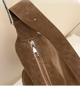 Detail view of smooth silver metal zipper and neat stitching on brown suede handbag