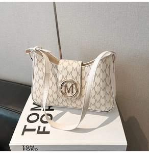 Detailed side view of beige monogram shoulder bag with gold metal buckle on a white book