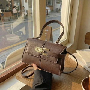 Elegant brown trapezoid leather handbag with gold turn-lock closure on wooden table