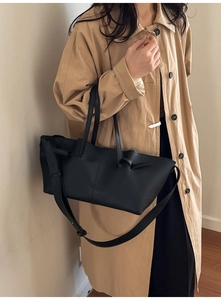 Detail of a black pleated tote bag with knot handles and adjustable shoulder strap