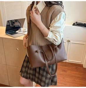 Detail of a brown leather tote bag with side drawstring accents and slender handles