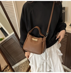 Close-up of brown lychee grain leather handbag with gold twist lock on model