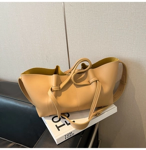 Detail of beige pleated tote bag showing drawstring knots and vibrant yellow interior