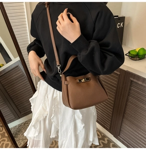 Detailed view of brown litchi pattern leather handbag with gold twist lock and long strap