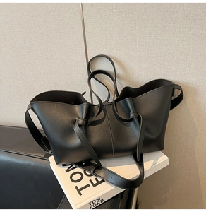 Detailed close-up of black matte leather tote bag with unique pleated texture and side knot
