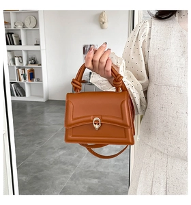 Detail of caramel leather handbag featuring a knotted handle and golden buckle clasp