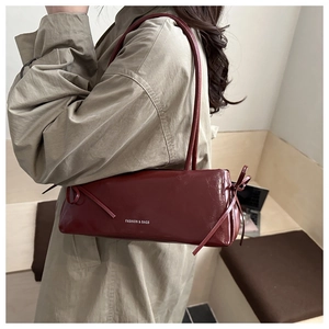 Gros plan d'un sac baguette en cuir rouge foncé avec détail de nœud latéral sur un mannequin