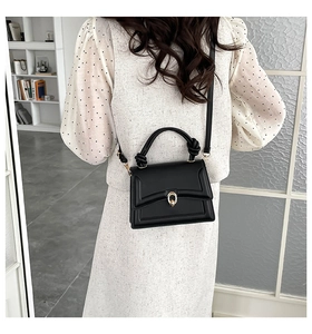 Detail view of a black structured crossbody bag with gold twist lock and knotted handle