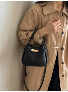 Sac seau élégant en cuir grainé noir avec fermoir doré porté par un mannequin en trench beige