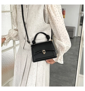 Detail of black mini crossbody bag featuring a golden buckle and stylish knotted handle