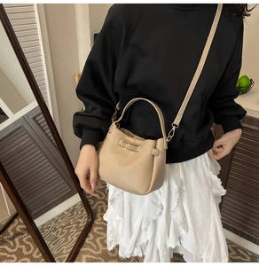 Close-up of a beige bucket bag with litchi grain texture and a twist lock buckle