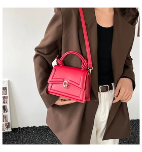 Detail of red crossbody bag with knotted handle and gold U-shaped buckle on model
