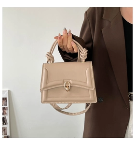 Detail of beige handbag featuring knot handle design and gold twist lock closure