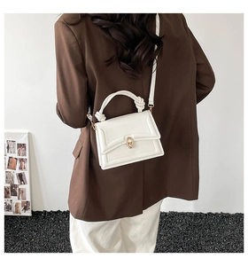 Close-up of white crossbody bag with knot handle and golden metal buckle on a model