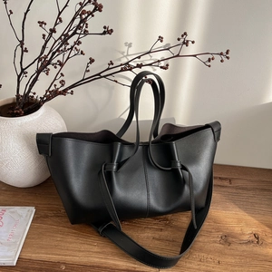 Black pleated leather tote bag with dual handles and shoulder strap on wooden table