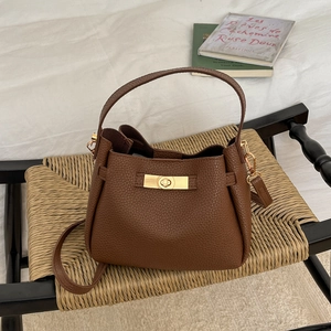 Sac seau marron en cuir grainé avec fermoir doré sur un tabouret en paille