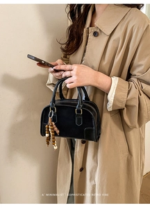 Dettaglio di borsa retrò nera con ciondolo in perline di legno tenuta da una modella