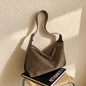 Retro coffee brown suede shoulder bag with wide strap and silver buckle on wood chair