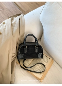 Dettaglio borsa Boston nera retrò con hardware dorato su un libro e un trench