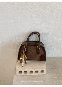 Dettaglio borsa boston in camoscio marrone scuro con nappa in legno su base in pietra