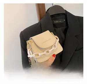 Close-up of beige mini square bag featuring chunky white acrylic and gold metal chains