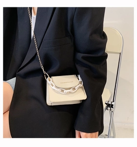 Detail of beige mini square bag with dual chain straps worn by a model in casual attire