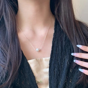 Pendentif en perle élégant sur une fine chaîne serpent portée par une femme