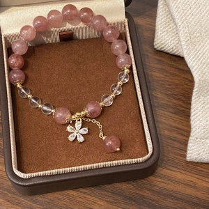 Pink natural stone beaded bracelet with gold flower pendant on wooden background
