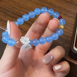 Détail d'un bracelet en perles bleu clair avec une perle rouge et des fleurs blanches