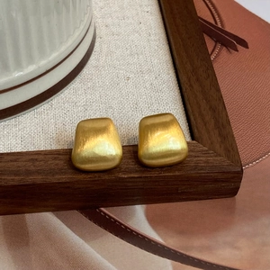 Macro detail of trapezoid gold earrings with brushed matte finish on a tray