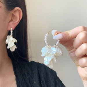 Elegant white floral earrings with pearl drop and gold metallic details on a model