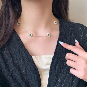 Gold chain necklace with white pearl flower charms and green beads worn by a model