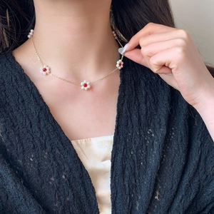 Handmade gold plated necklace with pearl daisy charms and red bead center on model