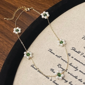 Gold-plated floral chain necklace with white pearls and green bead accents on a wood base