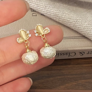 Details eleganter Schmetterlingsohrringe mit Champagner-Opal und Barockperlen auf warmem Grund