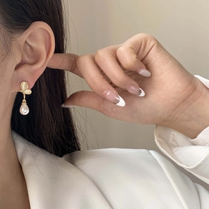 Close-up of golden butterfly earring with elegant white teardrop pearl on female ear