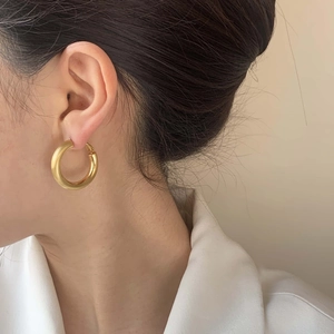 Gros plan de grandes boucles d'oreilles créoles dorées portées avec une chemise blanche
