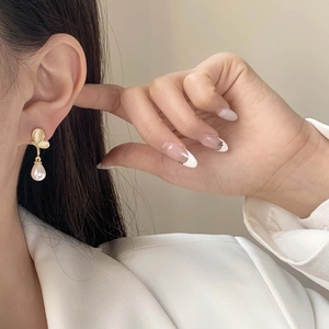 Elegant gold-edged pearl drop earrings featuring a leaf design on a female model