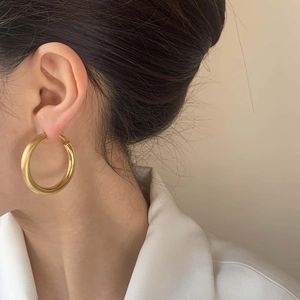 Gros plan de boucles d'oreilles créoles dorées épaisses au fini poli portées sur un modèle
