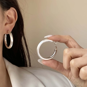 Détail de boucles d'oreilles créoles argentées avec fini satiné et bords polis sur modèle