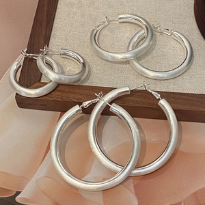 Trois paires de créoles en argent mat de tailles variées sur un présentoir moderne