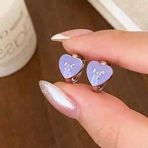 Detail of silver heart earrings with purple enamel and a tiny bow worn on hand