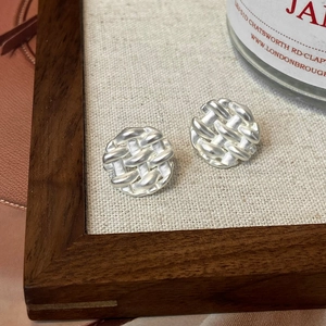 Macro view of silver woven texture disc stud earrings on a walnut tray with linen