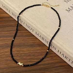Detailed close-up of beaded black spinel necklace with golden moon pendant on a book