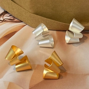 Macro view of minimalist matte gold and silver geometric spiral ribbon stud earrings