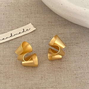 Macro view of matte gold irregular ribbon twisted earrings on rustic linen background