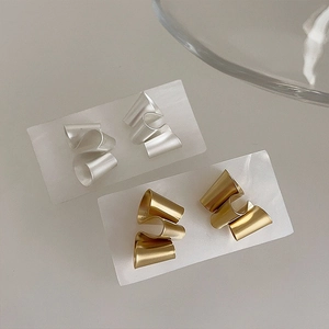 Detail of twisted geometric matte earrings in gold and silver with brushed texture
