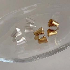 Detail of twisted matte geometric earrings in gold and silver finish on glass tray