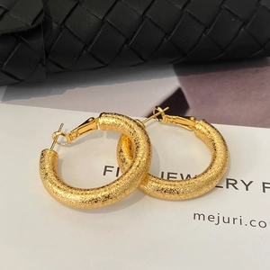 Detail of gold hoop earrings with frosted sandblast finish and needle clasp closure