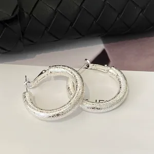 Close-up of large silver geometric hoop earrings with a matte frosted sand texture